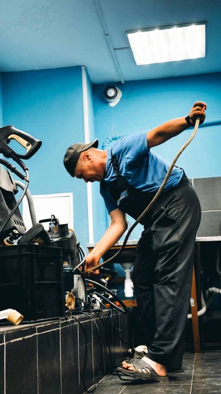 A technician in blue attire repairing equipment in an indoor workshop setting.